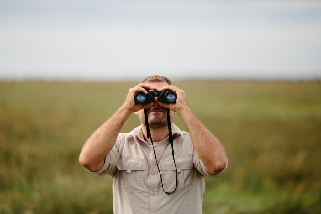 Man using binoculars in a grassy field.