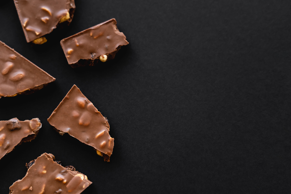 Pieces of chocolate with nuts on a black background, arranged in the lower left corner.