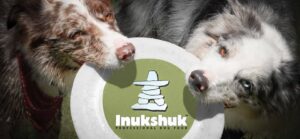 Two dogs pull on a frisbee with the Inukshuk Professional Dog Food logo in the center.
